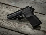 Czarny pistolet P.M.G.-23 leżący na zniszczonej drewnianej desce.