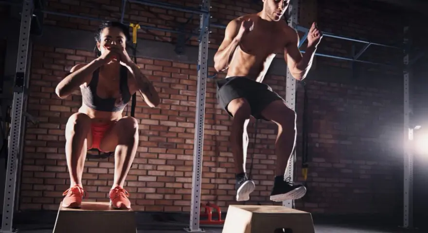 Para ćwicząca CrossFit wykonuje skoki na skrzyni w siłowni.