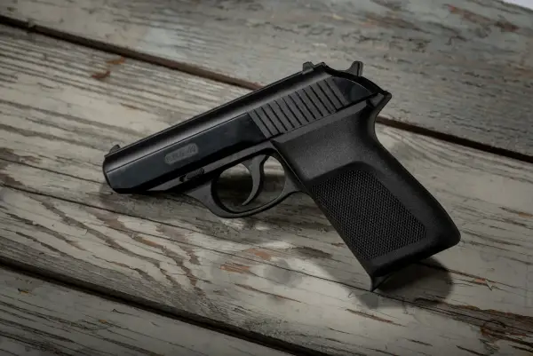 Czarny pistolet P.M.G.-23 leżący na zniszczonej drewnianej desce.